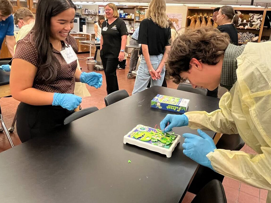 People in a laboratory wear gloves while examining a green sample on a tray.