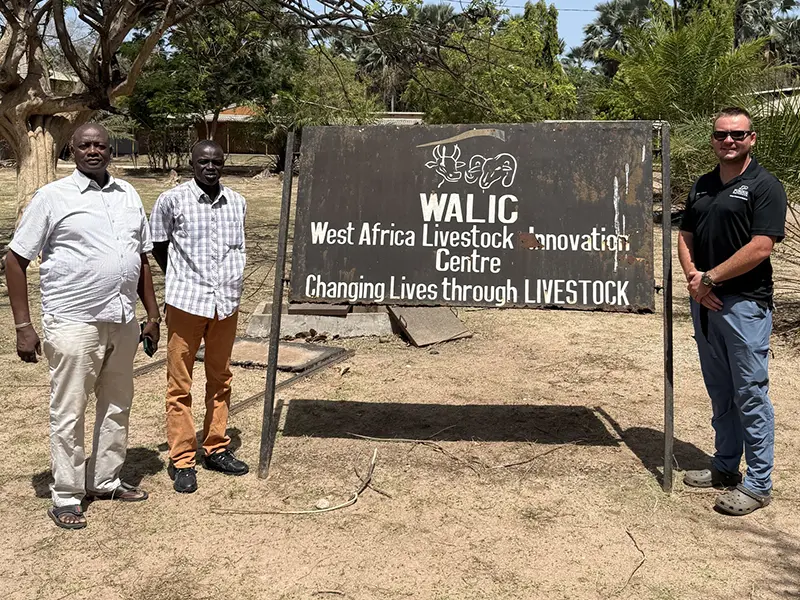 Three men stand beside a sign for the West Africa Livestock Innovation Centre.