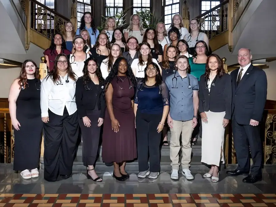 A large group poses on a grand staircase, with several people wearing stethoscopes and medical attire.