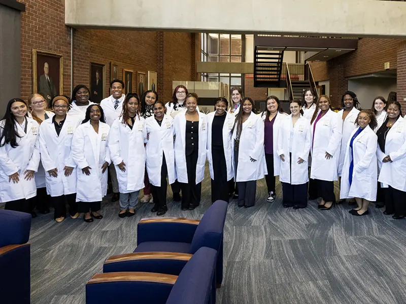 Group of people in white lab coats posing together in a brick-walled atrium.