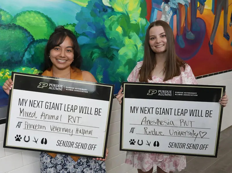 Two smiling women hold signs describing their next career steps: mixed-animal veterinary technician at Princeton Veterinary Hospital and anesthesia veterinary technician at Purdue University.