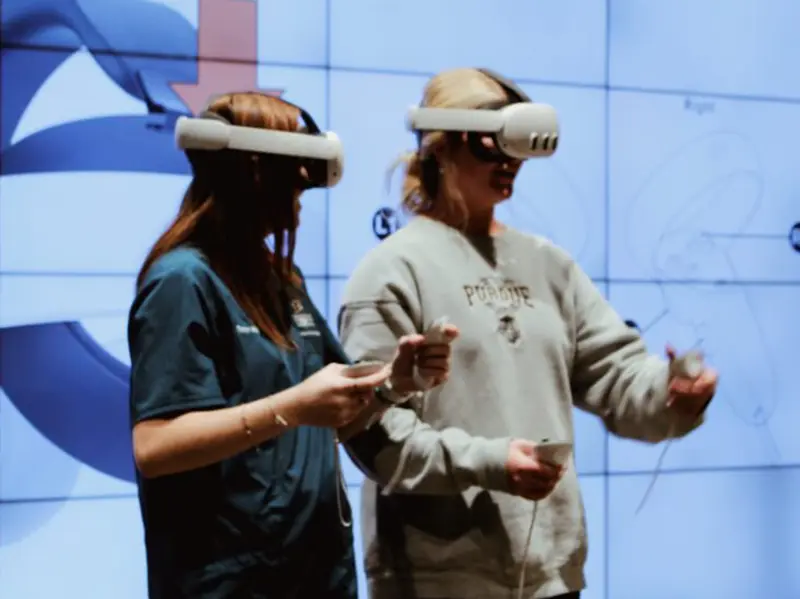 Two people wearing white mixed-reality headsets interact with a virtual display.