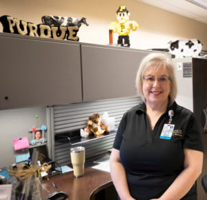 A smiling woman stands in an office setting, surrounded by playful decorations related to a school theme.
