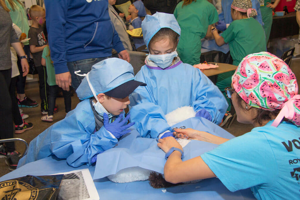 Kids pictured in scrubs examining a stuffed animal