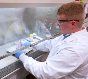 A man in a lab coat works at a laboratory bench within a fume hood, focusing on scientific experiments.