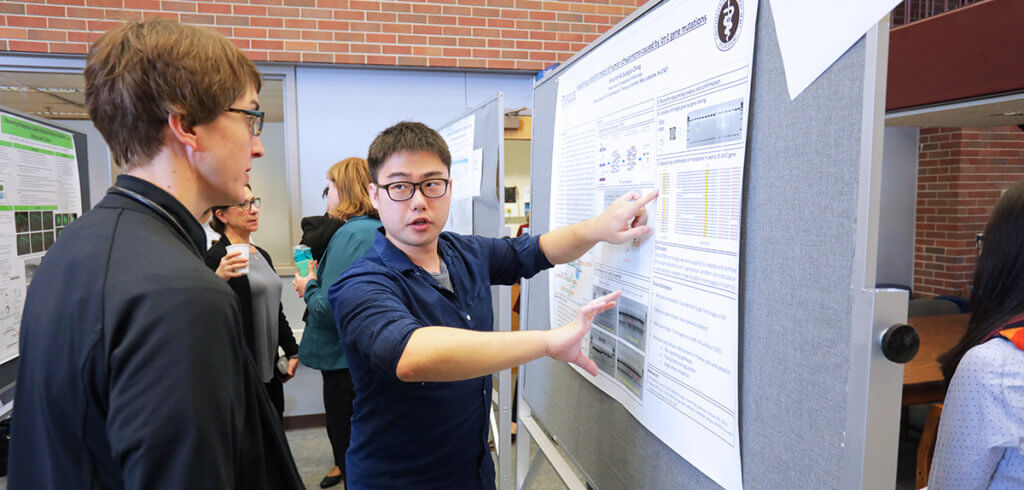 graduate student discusses research on his displayed poster with faculty member