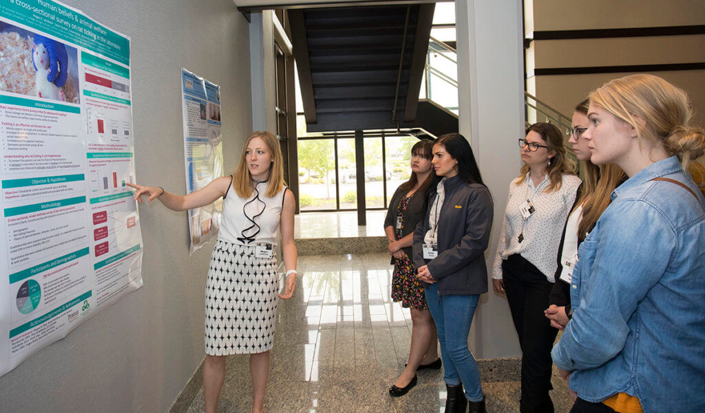 Megan points to her research poster as partipants listen