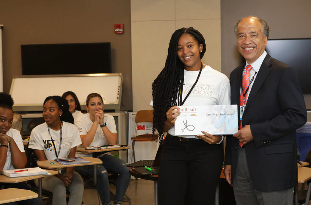 Candis holds up her new stethoscope next to Dean Reed as additional Vet Up! College participants look on