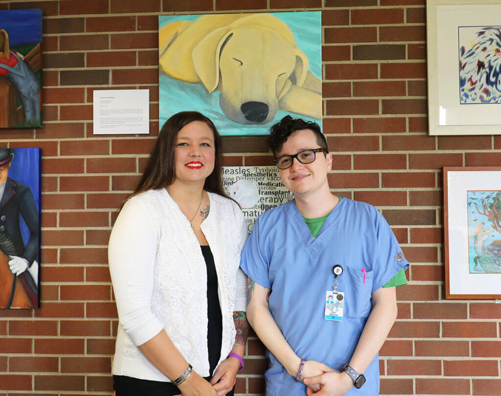 Hanna and Eric stand for a photo together against a wall of artwork in Lynn Hall