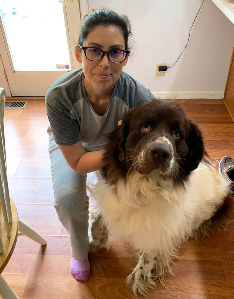 Vanessa kneels beside her dog, Titan, at home