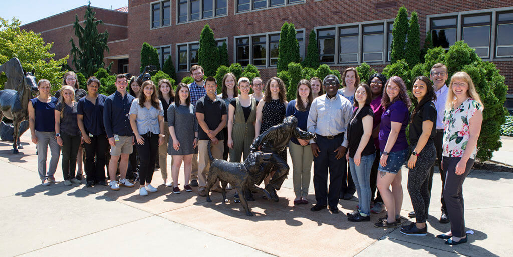 summer research program participants gather aound the Continuum sculpture in front of Lynn Hall