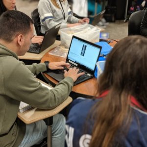 A group of students collaborates around a table using laptops.