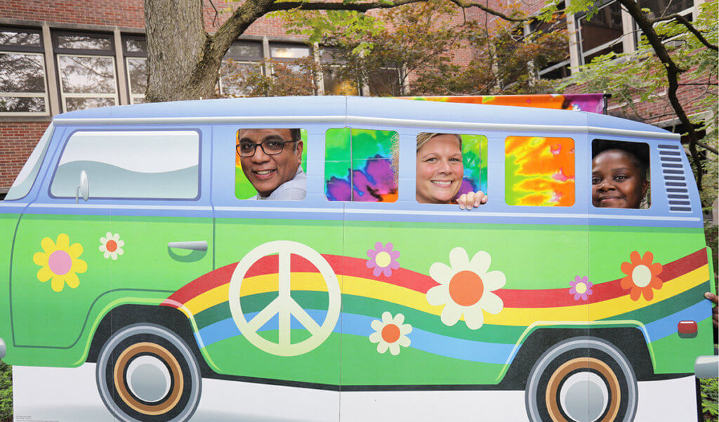 Dr. Narayan, Julie, and Tempess stand behind a 60s van photo prop at the appreciation event