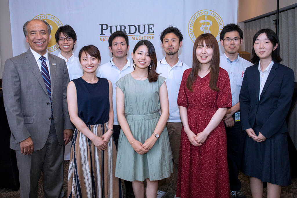 Kitasato students and faculty advisor join Dean Reed for a group photo against the college's logo backdrop