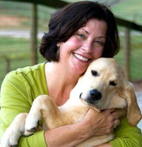 A woman is smiling while holding a golden retriever puppy in her arms.