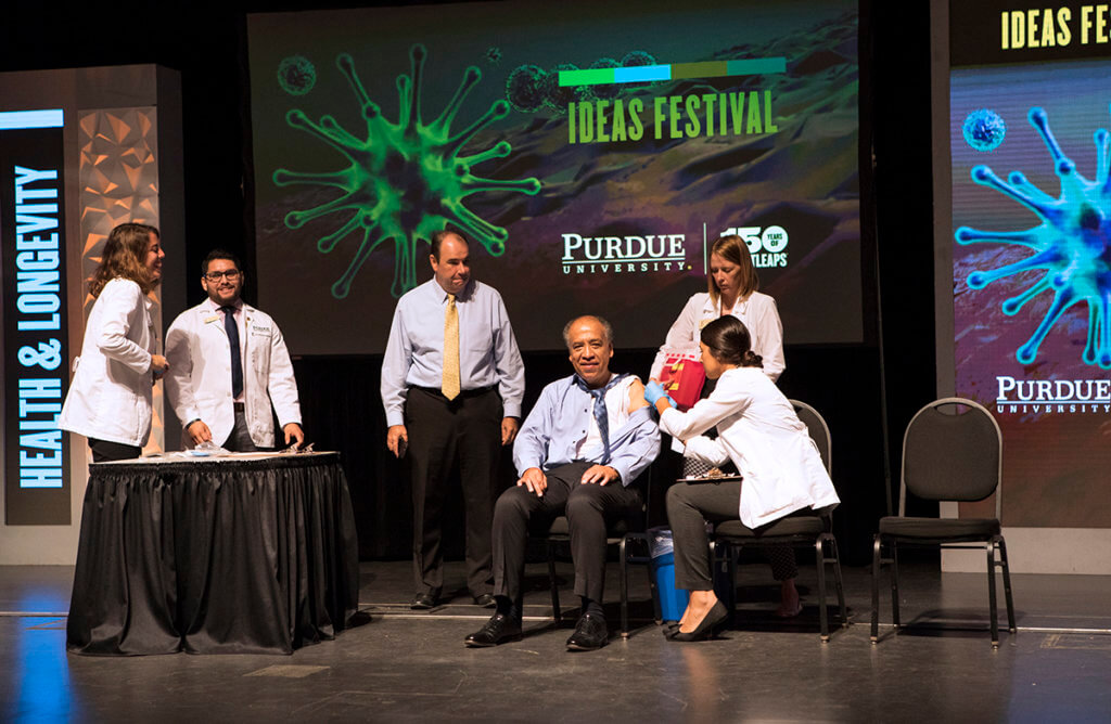 Dean Reed receives a flu shot in his arm while seated on stage