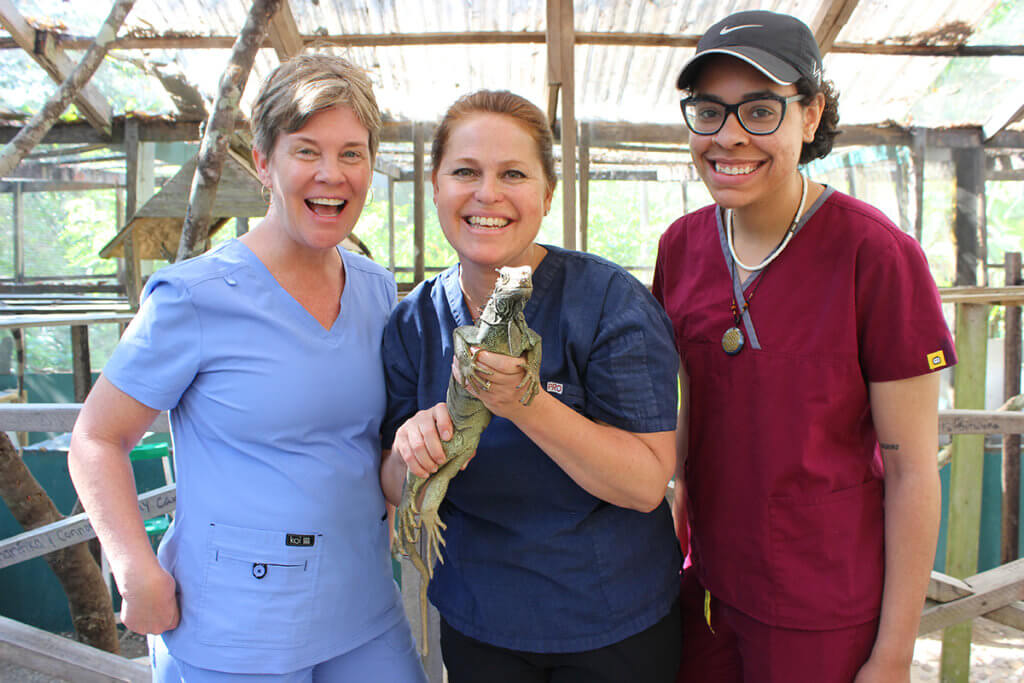 A global CE participant smiles holding a large iguana with fellow particpants standing beside her
