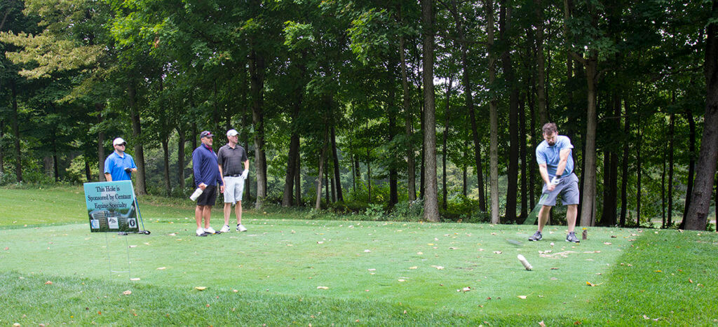 A golfer takes a swing as his teammates watch from the sidelines