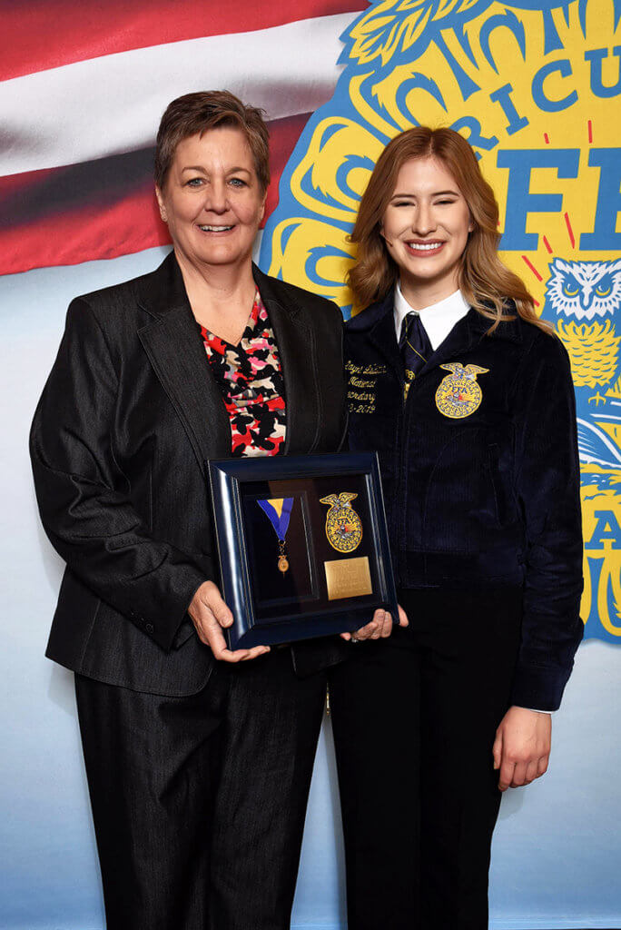 Paige stands beside Layni holding her award plaque