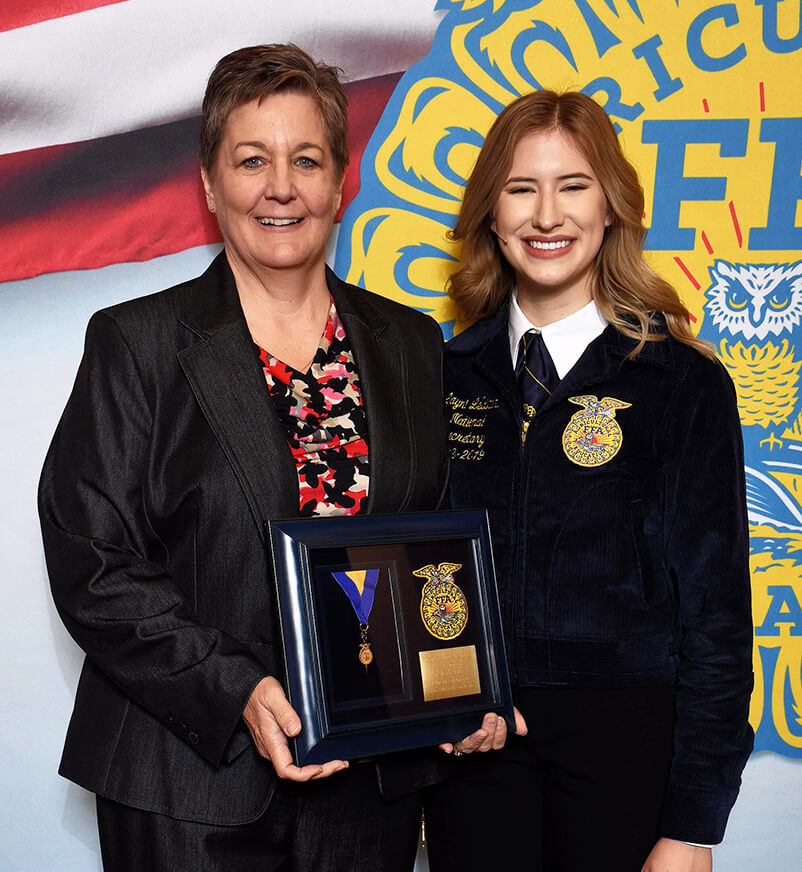 Paige stands beside Layni holding her award plaque