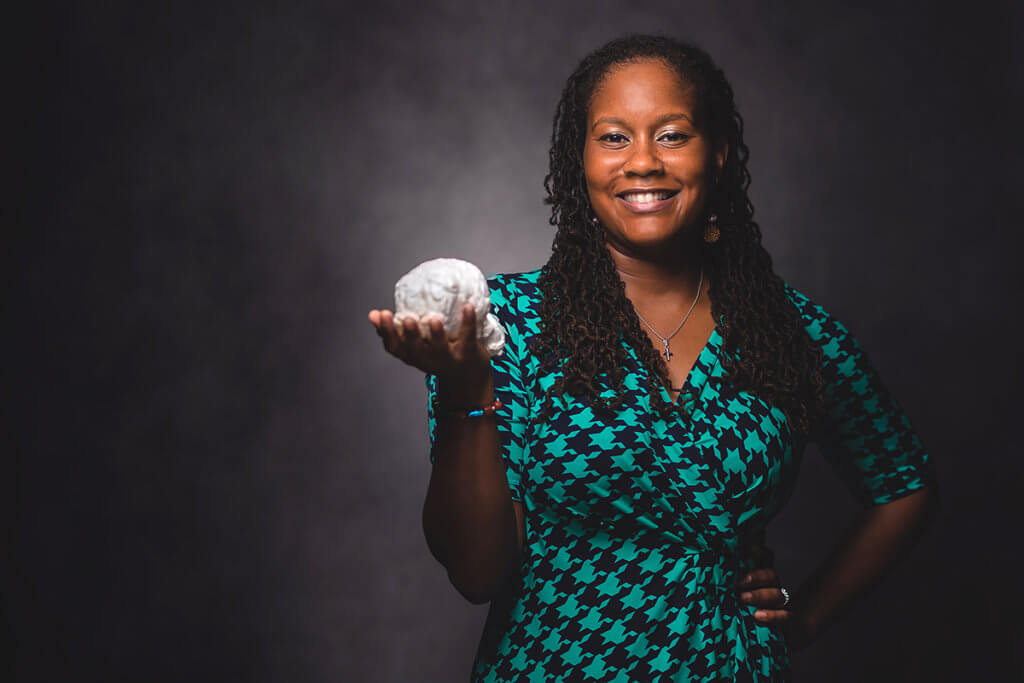 Dr. Lyle pictured against a photo backdrop holding a model of a brain