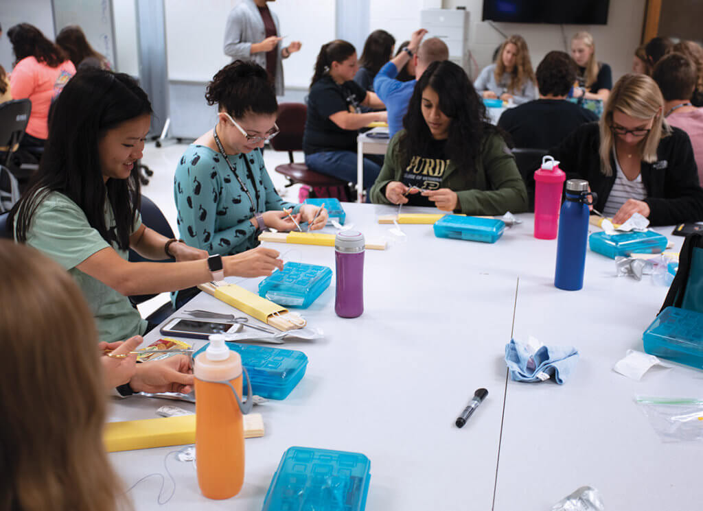 Students sit in table groups practicing suturing