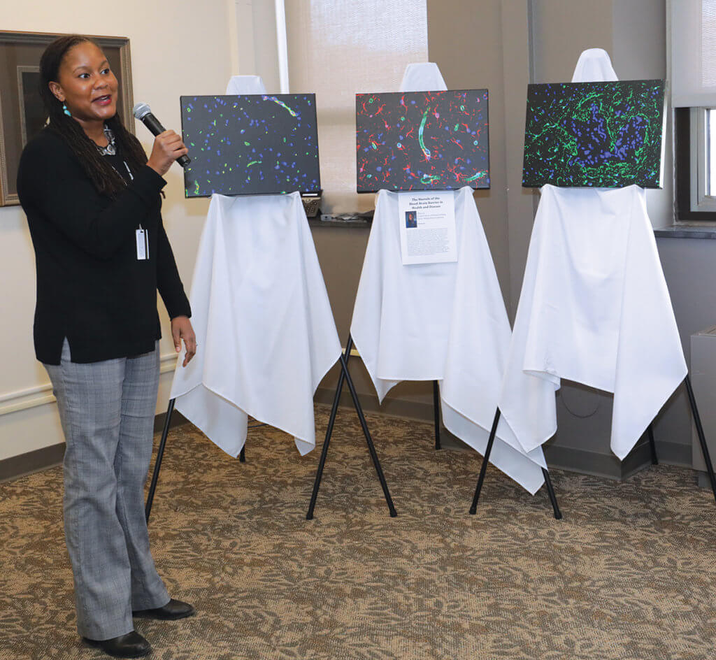 Dr. Lyle speaks into a microphone next to the three canvas prints