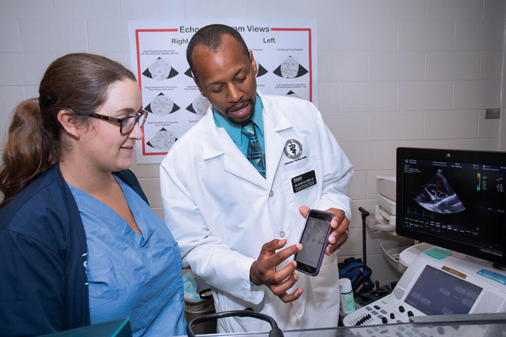 Dr. Green holds a cell phone showing the screen to Taylor