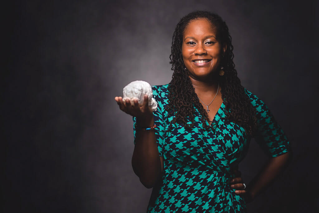 Dr. Lyle stands against a gray photo backdrop holding a white model of a brain