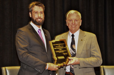 Matt and Jerry stand together holding Jerry's award plaque