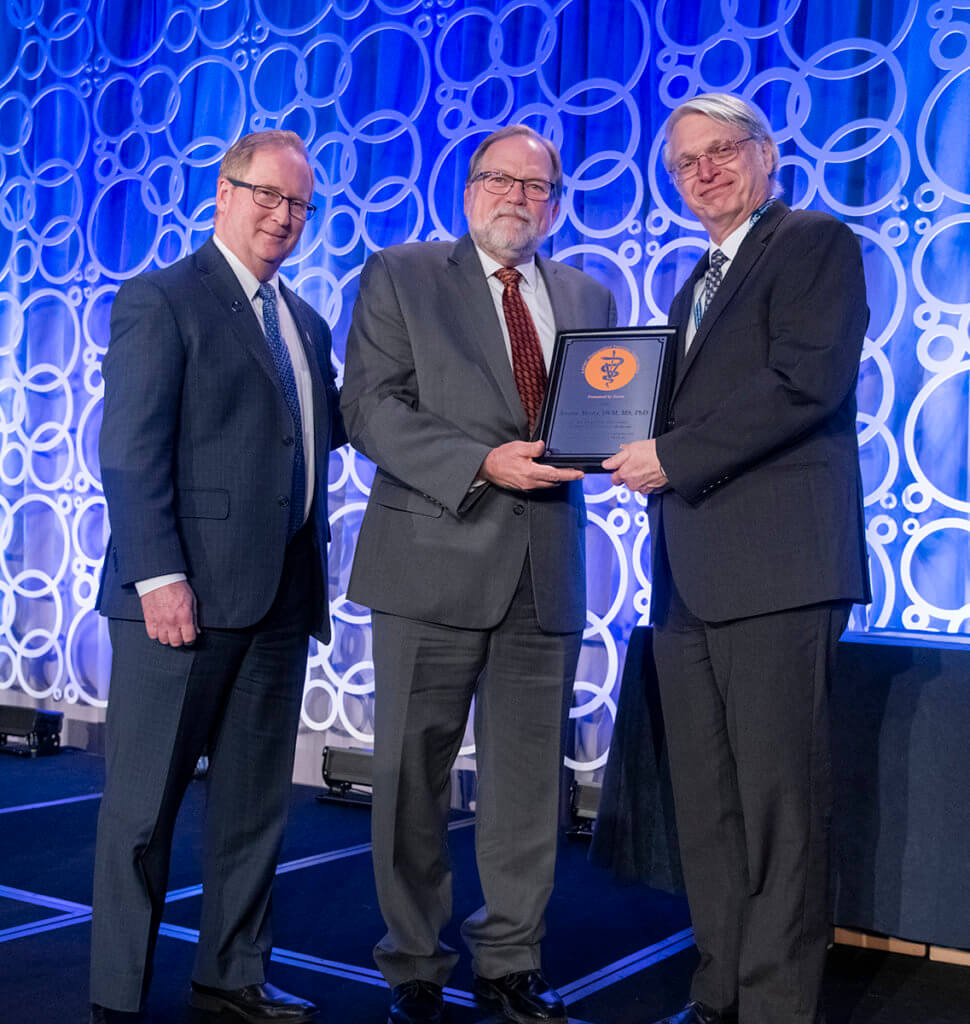 Dr. Masty is presented with his award plaque on stage at AAVMC