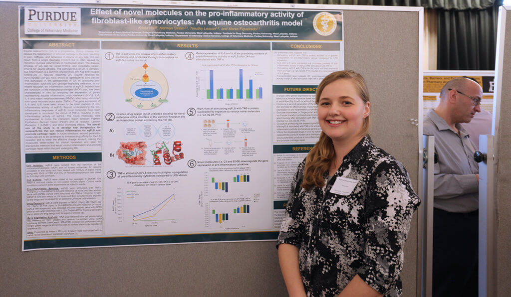 Krista stands smiling in front of her research poster