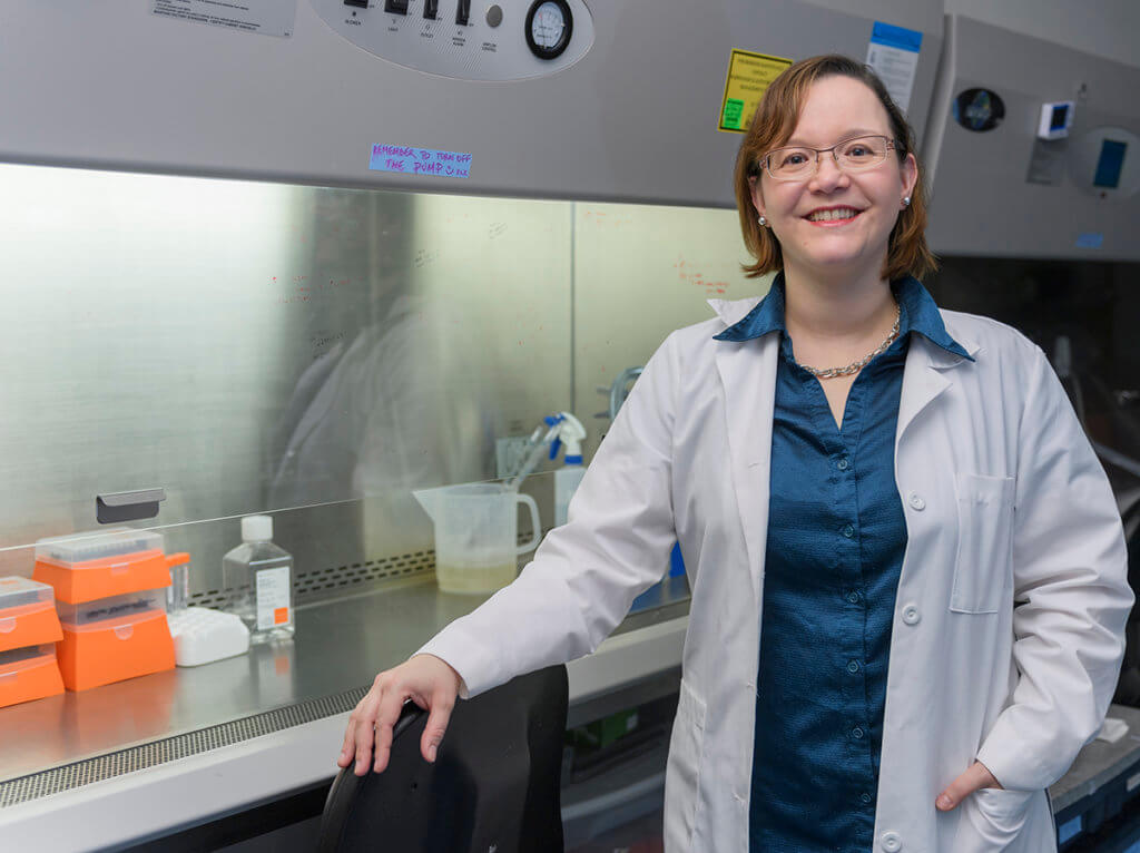 Marxa stands with her arm draping the back of a chair in her lab