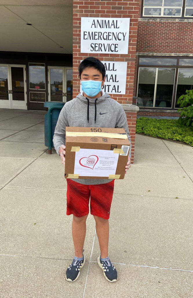 A boy wearing a facemask holds a box in front of the Small Animal Hospital