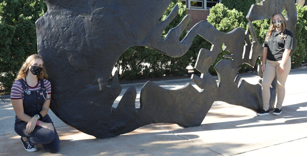 Brooke and Hannah stand socially distanced beside the Continuum sculpture outside Lynn Hall