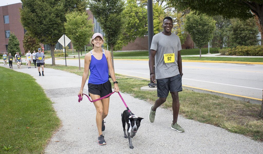 dog jog participants walk along the path with their dog as other participants follow in the background