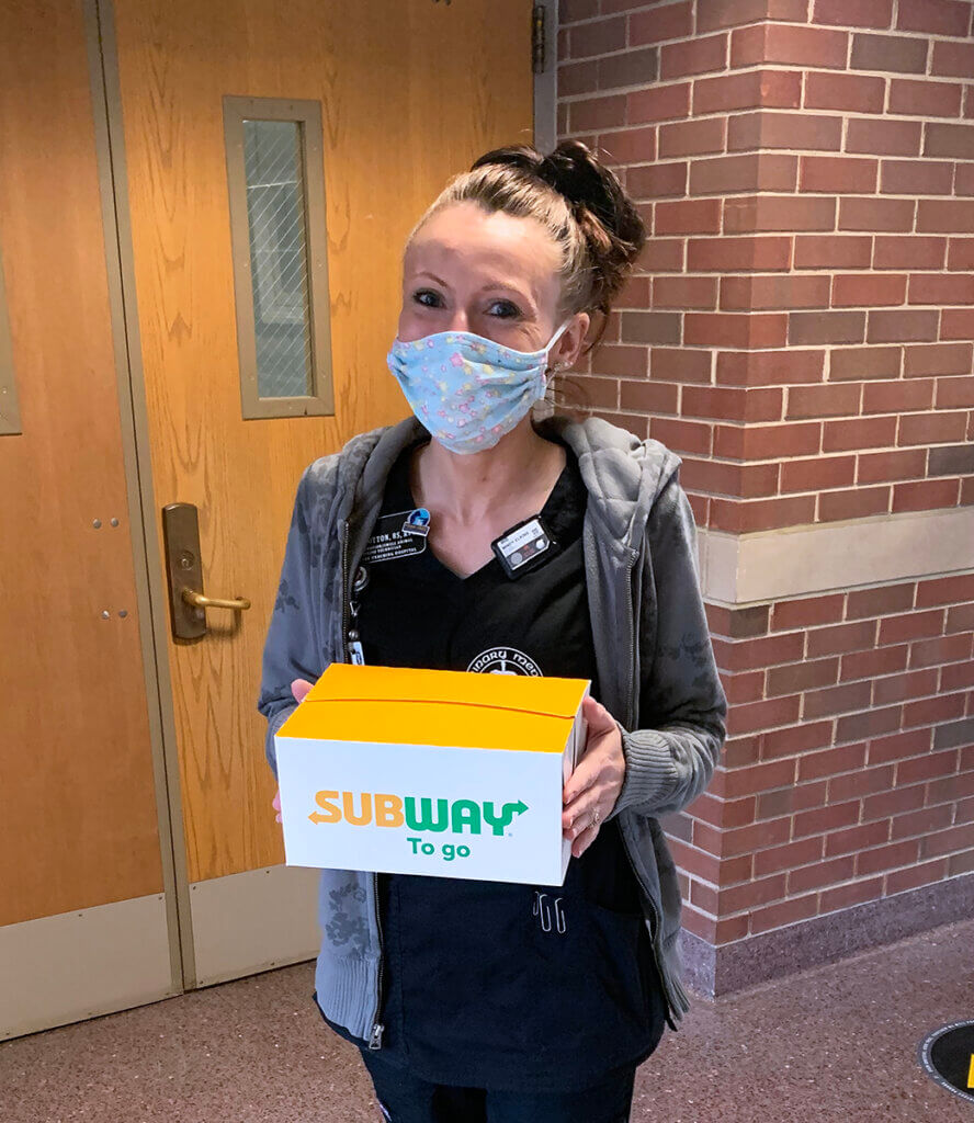 Mindy wears a face mask and holds up her subway to go box lunch in Lynn Hall