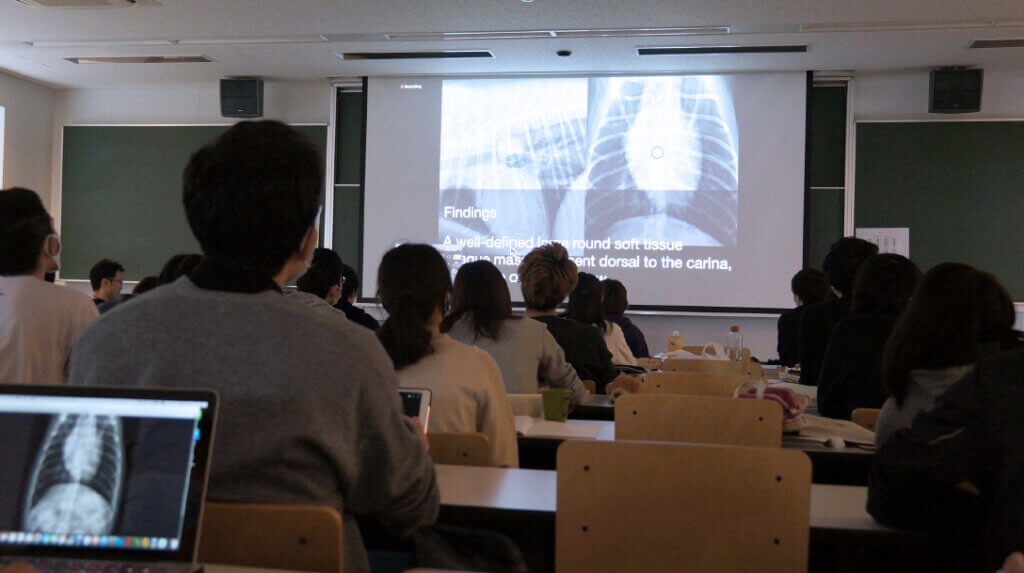 View from the back of a classroom in Japan as students watch the presentation projected on a screen at the front of the class