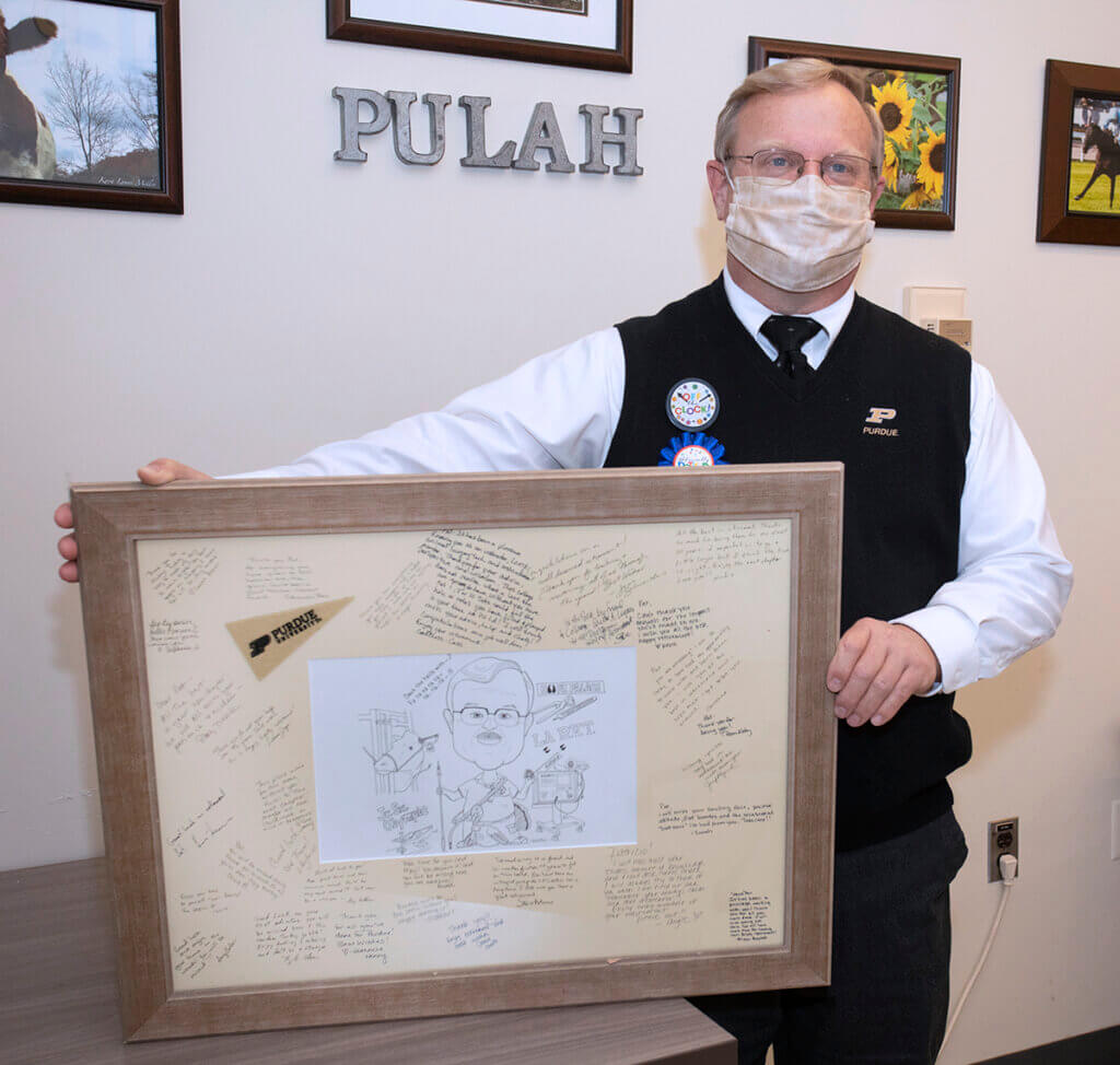 Pat holds up the framed caricature. He's wearing celebratory retirement pins on his vest.