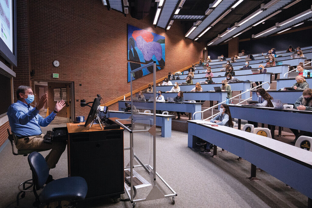 Dr. Turek sits behind a plexiglass shield as students sit distanced in the lecture hall