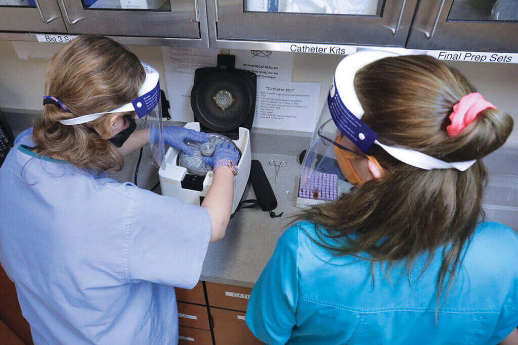 Students wear face shields and masks as they place samples in a machine