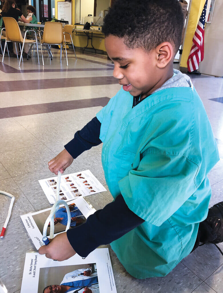 A young boy sits on the floor wearing a surgical scrubs working on an activity