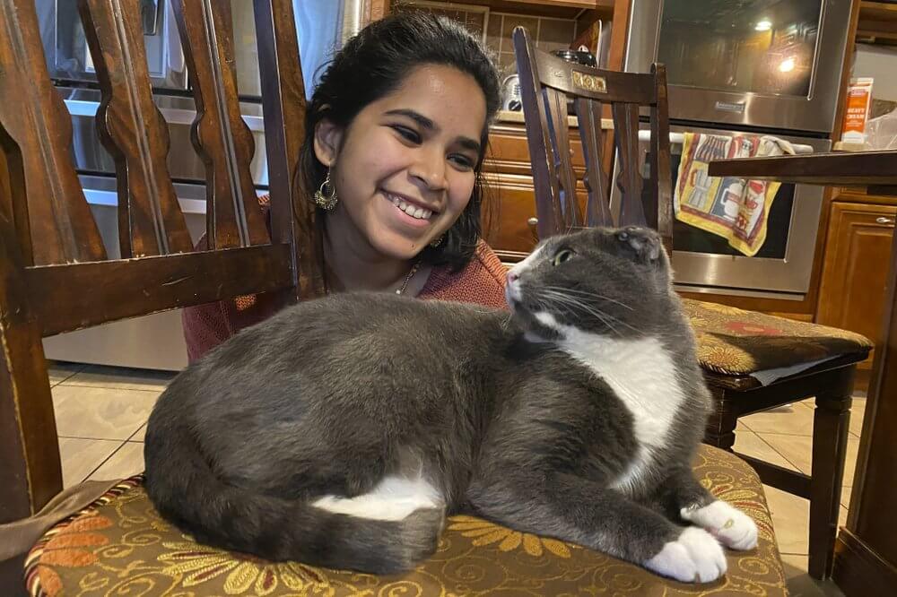 In this photo provided by Raghav Ranjan, Devika Ranjan smiles at her cat, Aloo, on Dec. 13, 2020, in Andover, Mass. Ranjan, a theater director in Chicago, wanted pandemic company and got a rescue cat she named Aloo during the summer. The formerly feral cat is believed to be around 3, and seems to be very comfortable with a slow-paced, high-attention pandemic life. “My working from home, I think he loves it,” she says. “I think he is just ready to settle down in life. If he were human, he'd probably sit on the couch with a PBR (beer) and watch TV all day." (Raghav Ranjan via AP)