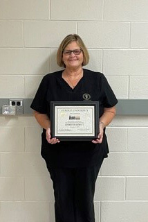 Jennifer holds up her Bravo Award certificate in a hallway of the hospital