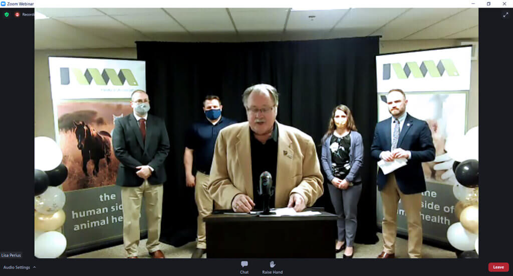 Dr. Schnarr pictured in front a lectern with others in the background as viewed over Zoom