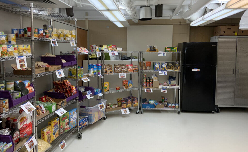 shelves line the walls with organized groups of food and displayed next to a refrigerator and freezer