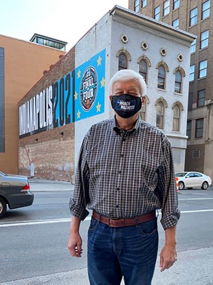 Dr. Borst stands in front of a Final Four basketball mural on a building in downtown Indianapolis, while wearing a March Madness face mask