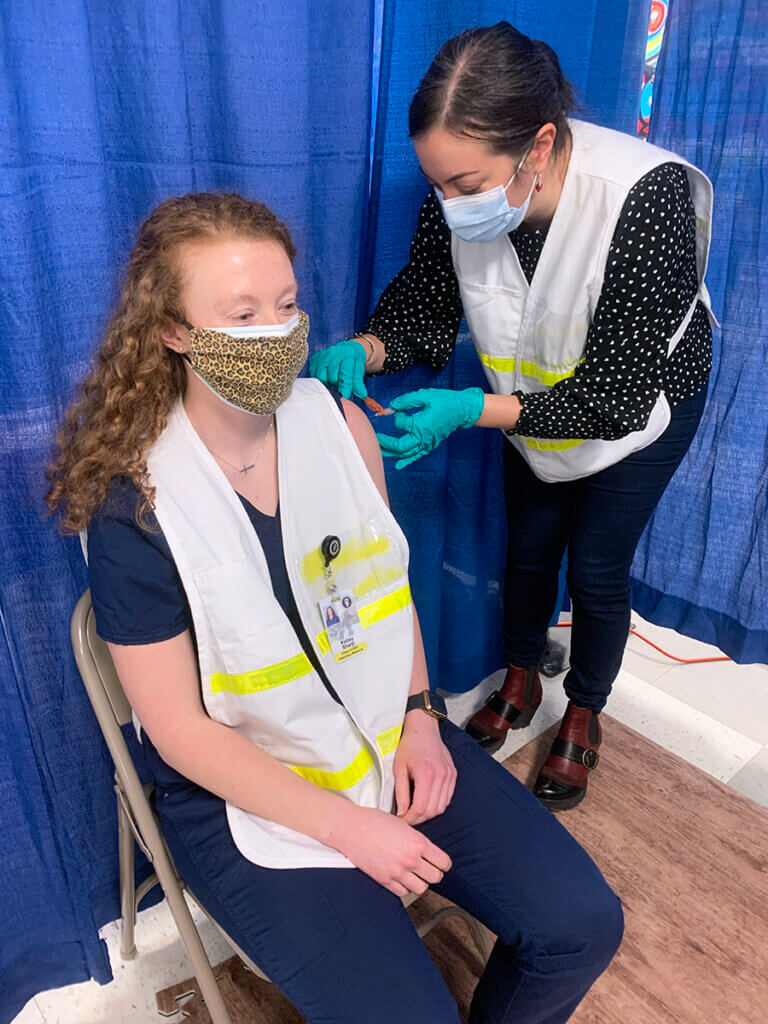 Kelley sits as Dr. Malek gives her a vaccine shot in her left arm