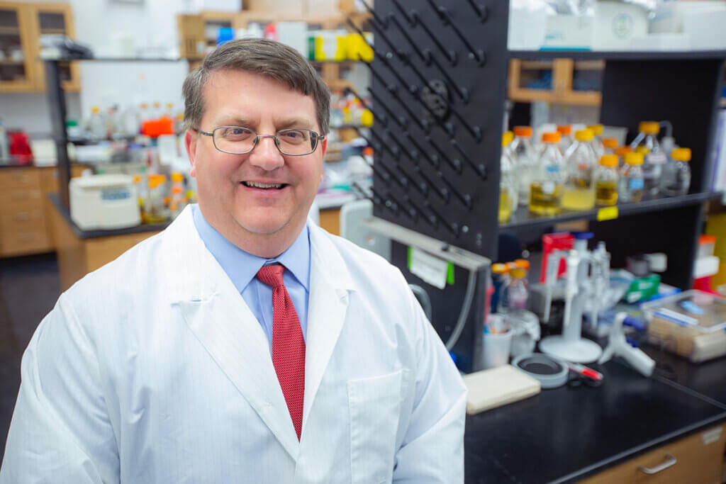 Paul Plummer smiles wearing a white lab coat in a lab