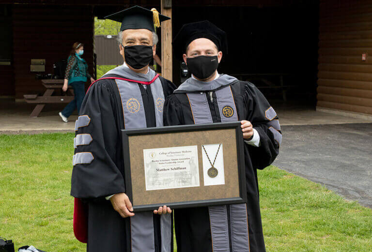 Matthew and Dean Reed wear facemasks and hold us his award plaque